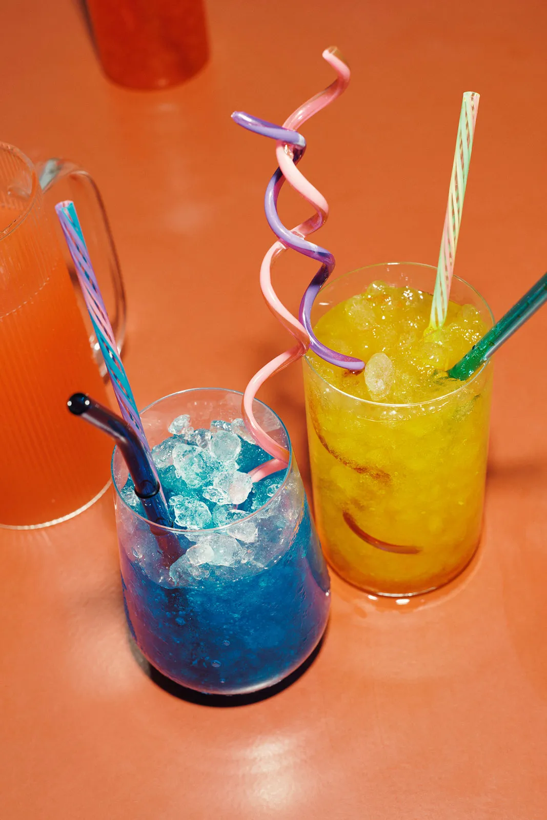 giacobbe_juli-2025-6 Twee kleurrijke drankjes met rietjes op een oranje tafel.